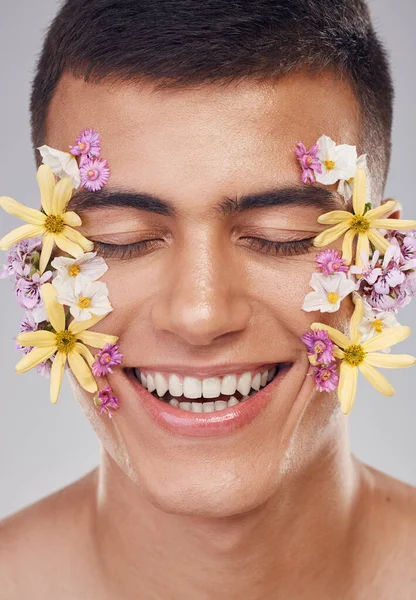 Relax, face or happy man with flowers for beauty, natural cosmetics or wellness in studio on white background. Nature aesthetic, smile or model laughing at eco friendly skincare or spring floral art.