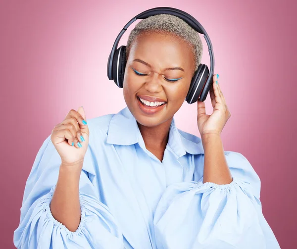 Headphones, dance and happy black woman in studio with music, radio or streaming subscription on pink background. Podcast, earphones or African lady model dancing to album track or feel good playlist.