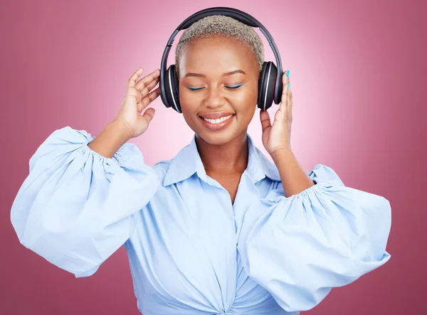 Music, headphones and happy black woman in studio for radio, streaming or audio subscription on pink background. Podcast, earphones and African lady model smile for album track or feel good playlist.