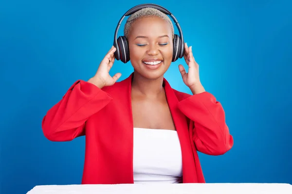 Music, headphones and black woman dance in studio celebration with news, feedback or promo on blue background. Freedom, happy and African model dancing to earphones radio, podcast or audio streaming.