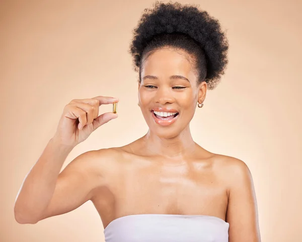 Skincare, smile of black woman and fish oil for beauty isolated on a brown background in studio. Happy, natural cosmetics and omega 3 supplements, biotin or vitamin pills of African model for health.
