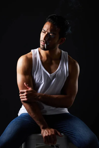 Smoking, thinking and sexy man on chair in studio in fitness, beauty aesthetic and sensual fashion. Erotic art, sexual body and male model with muscle, cigarette and black background in dark lighting.