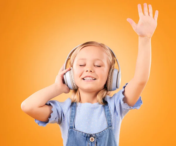 Headphones, happy or child streaming music to relax with freedom in studio on orange background. Hand up, singing or girl singer listening to a radio song, sound or gospel on an online subscription.
