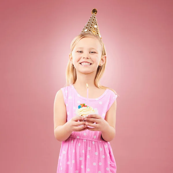 Cupcake, birthday and portrait of a child with a hat for holiday party or happy celebration. Excited girl on a pink background for surprise, cake or celebrate achievement with a dessert and joy.