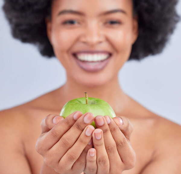 Apple, black woman and hand closeup with health, diet and natural skincare glow in studio. Happy, face and fruit for healthy nutrition, grey background and wellness with a smile from organic food.