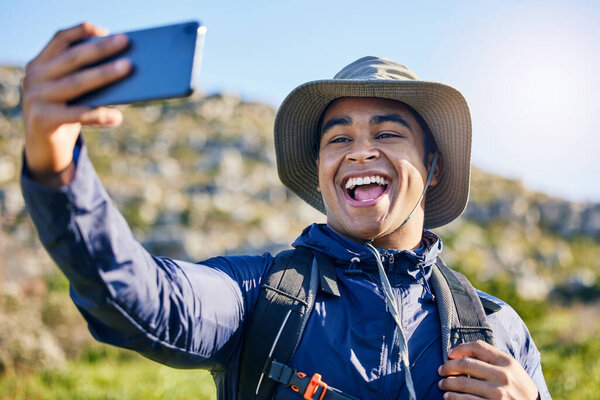 Selfie, freedom and a man hiking in the mountains for travel, adventure or exploration in summer. Nature, smile and photography with a happy young hiker taking a profile picture outdoor in the sun.