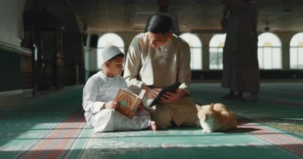 クルアーンと子供と人間は アッラーのために祈り 平和と霊的ケアをモスクで教えています 本を読む タブレットを持つイスラム教徒の人 子供や教育 神を崇拝するのを助けるために — ストック動画
