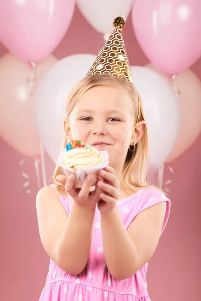 Balloons, birthday and portrait of child with cupcake for holiday, happy celebration and fun party. Young girl kid on a pink background for surprise, cake or celebrate achievement with a dessert.