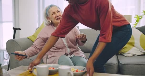 周末早上 在一个现代化的家庭里 早餐和一位老年妇女坐在沙发上 在客厅里 快乐的咖啡和拥抱老年女性的非洲女孩一起享用着食物 — 图库视频影像