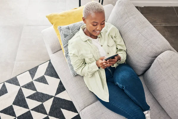 Woman, relax and typing with phone on sofa for social media, chat and online contact at home from above. Happy african person, smartphone and download mobile games, digital multimedia and dating app.