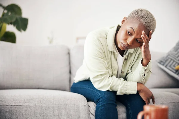stock image Woman, depression and thinking in home of pain, mental health or anxiety of debt, regret or risk. Stress, worry and frustrated african person with headache of sad trauma, broken heart or ptsd on sofa.