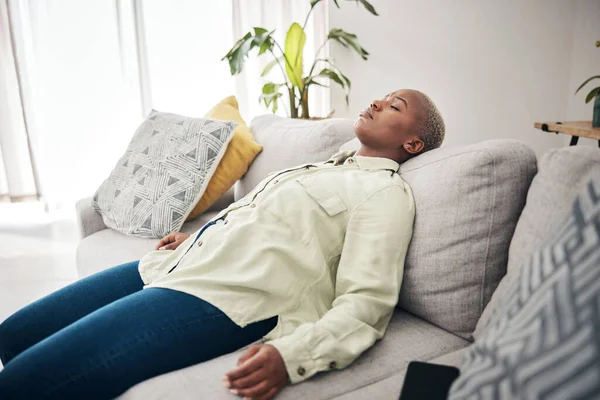 Tired, sleep and black woman on a home sofa for relax, stress relief or lazy after work. Mental health, living room and an African girl on a couch for rest, sleep or burnout with insomnia or fatigue.
