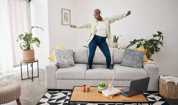Dance, black woman and listening to music on the sofa for freedom, the radio or an audio. House, streaming or African girl with headphones for a podcast, playlist or enjoying a song on the couch.