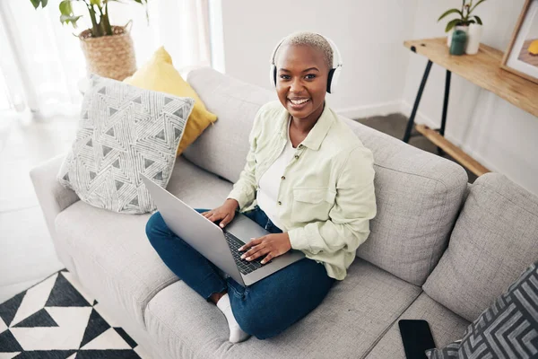 Portrait of black woman, remote work or laptop on sofa in living room for online research in headphones. Happy, top view or journalist working on computer for streaming or social media blog at home.