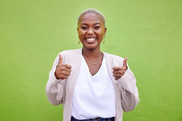 Happy, thumbs up and portrait of black woman by a green wall with classy and elegant jewelry and outfit. Happiness, excited and African female model with positive and confident attitude with fashion