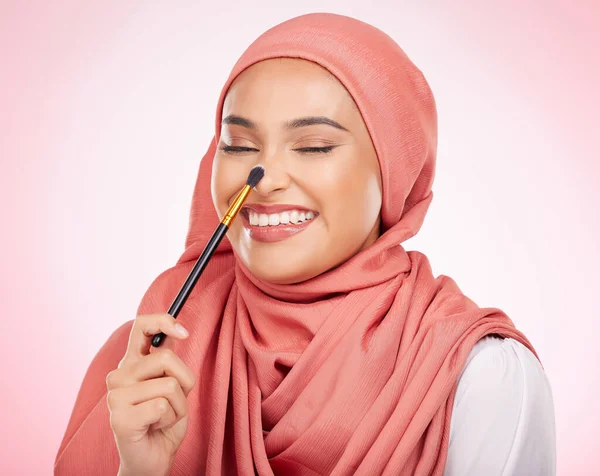 Makeup brush, relax face and happy Muslim woman with studio cosmetics tools, wellness routine or skincare shine. Product application, eyes closed and Arabic person with self care on pink background.