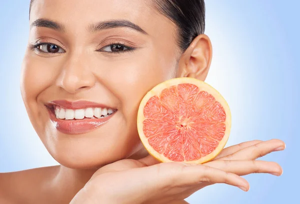 Portrait, beauty and grapefruit with a natural woman in studio on a blue background for health or wellness. Face, skincare and smile with a happy young model holding fruit for detox or antioxidants.