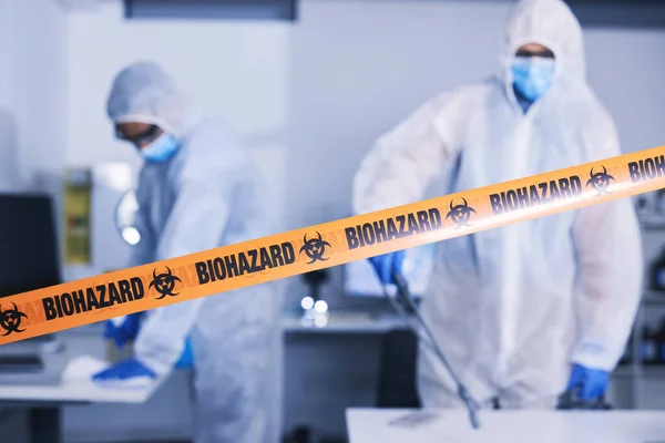 Hazard, tape and people in danger working with toxic, biology or team disinfect dangerous bacteria or health emergency. Biohazard, protection and medical staff in hazmat suit cleaning for bio safety.
