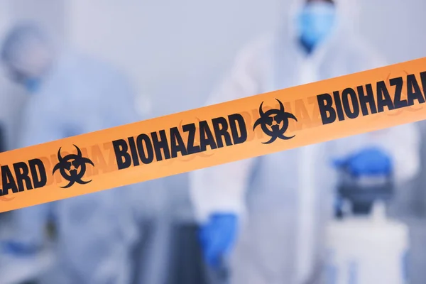 Biohazard, tape and people with caution working with toxic, biology or team disinfect dangerous bacteria for health crisis. Hazard, protection and warning for bio safety or cleaning in hazmat suit.