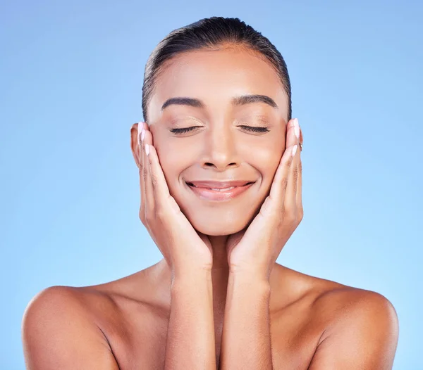 Skincare, peace and hands on face with happy woman in studio with blue background and dermatology or cosmetics. Indian, model and happiness with natural skin and healthy facial glow or beauty care.
