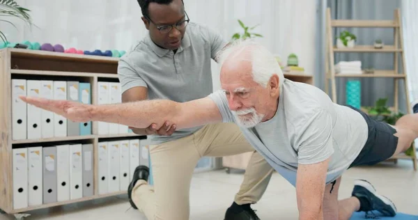 Physiotherapy, body stretching and senior man for rehabilitation, recovery and black man support client. Retirement physical therapy, mobility or African physiotherapist help elderly patient on floor.