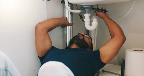 Plumber black man, kitchen and sink maintenance with tools, focus and pipe repair for drainage in home. Entrepreneur handyman, plumbing expert or small business owner in house for fixing water system.