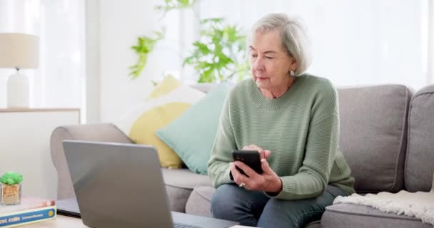 自宅で計画 投資調査 資産管理のウェブサイトのためのソファー上のシニア女性 ラップトップと電話 高齢者 財務情報や年金Faqのためにモバイルやコンピュータにタイピング — ストック動画