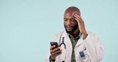 Stres, telefon ve doktor stüdyoda internetten tıbbi tedavi araştırması yapıyor. Baş ağrısı, hayal kırıklığı ve mavi arka planda cep telefonuyla teşhis üzerinde çalışan Afrikalı sağlık görevlisi.