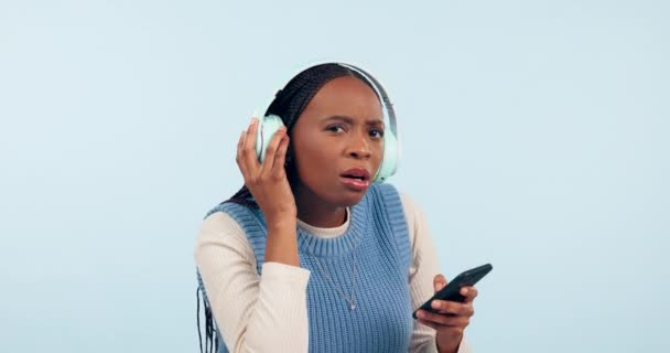 听到和面对黑人妇女与耳机在演播室说话 说话和说话 电话中的交流 干扰和人物形象 在蓝色背景下听音乐 歌曲或音频 — 图库视频影像