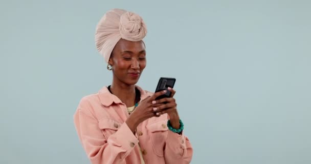 青いスタジオの背景に接続 タイピング ソーシャルメディアを備えたスマイル 黒人女性 スマートフォン アフリカの人 少女や携帯電話を持つモデル モバイルユーザーやデジタルアプリやネットワークで投稿 — ストック動画