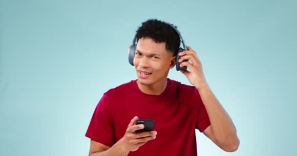 リスニング ヘッドフォン ダンス ストリーミングミュージックをブルースタジオの背景に スマートフォン デジタルアプリ エネルギーを備えたヘッドセット ヒアリング オーディオ付きのポートレート 人または幸せなモデル — ストック動画