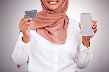 Kadın, kredi kartı ve telefon ekranı çevrimiçi alışveriş, müslüman moda pazarlaması ve atölyede ticaret. Beyaz arka planda ödeme için tesettür, mobil model ve bankacılık uygulaması kullanan İslami müşteri.