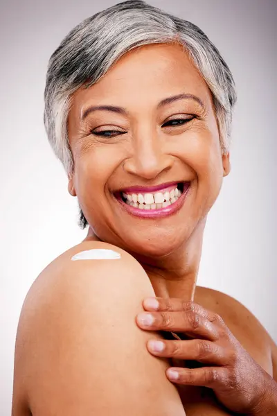 Body cream, shoulder and beauty of a mature woman with glow and smile on a white background. Dermatology, moisturizer and cosmetics of aesthetic model for skin shine, wellness or self care in studio.