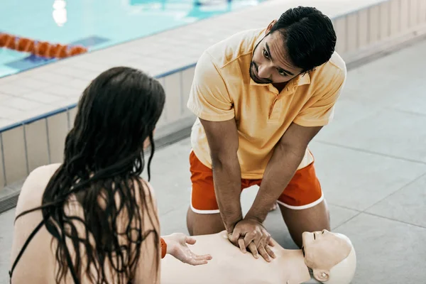 Swimming pool safety, first aid and man teaching life saving process rescue support or helping with danger. Client, emergency CPR and person learning medical service, lifeguard or practice on dummy.