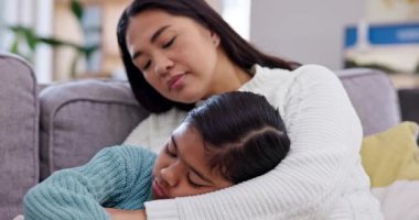 Rahatlık, bakım ve anne, aile evinin oturma odasındaki bir kanepede çocuğuna sarılıyor. Üzgün, bunalımlı ve Asyalı bir anne evinde kızını sevgi, destek ve şefkatle kucaklıyor.