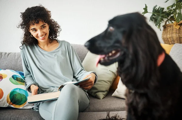 Reading a book, dog and a woman on home sofa to relax with animal in a living room. Pet owner, happiness and a young person on a couch with love, care and wellness or friendship in a cozy apartment.