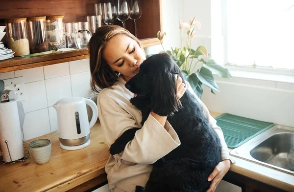 Hug, love and woman with a dog in home kitchen to relax and play with animal. Pet owner, happiness and asian person playing with companion, care and wellness or friendship in cozy apartment.