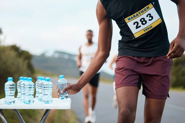 Hand, water and a marathon runner in a race or competition closeup for fitness or cardio on a street. Sports, exercise or running with an athlete grabbing a drink while outdoor on a road for training.