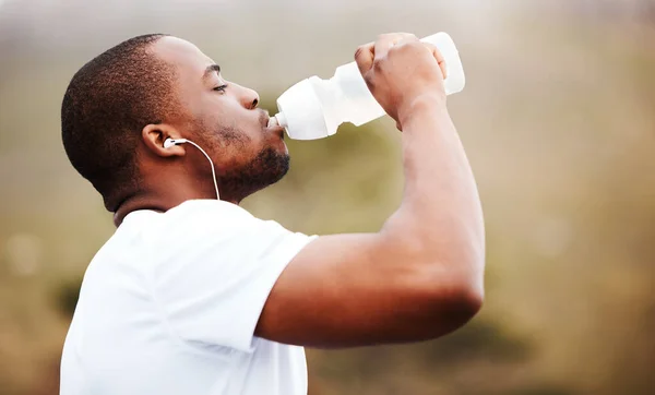 Black man, runner and drinking water with earphones, music or podcast, relax and fitness outdoor. Hydration, health and plastic bottle, listening to radio on run with exercise, mockup space and train.