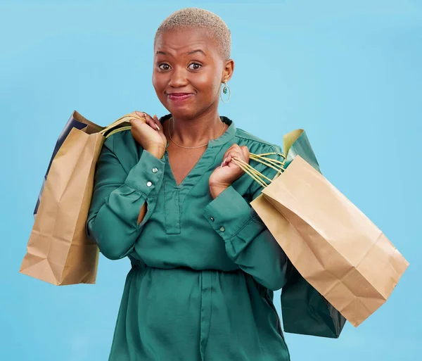 Woman, shopping bag and mistake in studio portrait for overspending, budget or deal by blue background. African girl, customer and regret for fail, stress or oops for gift, sale or retail addiction.