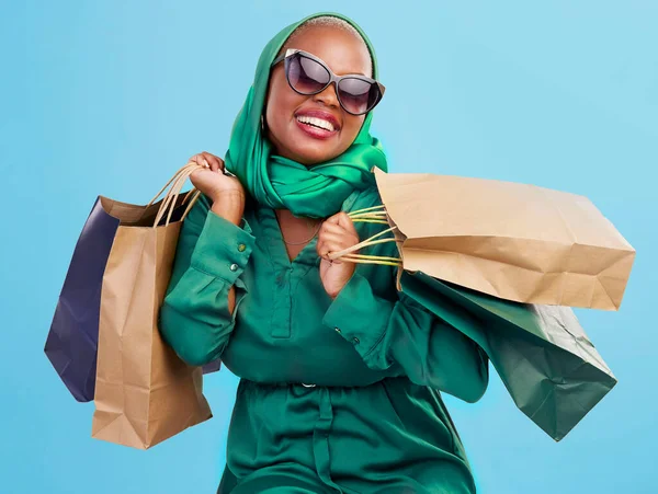 Shopping, sunglasses and black woman with bags, excited and boutique products on a blue studio background. African person, customer or model with luxury items, expensive clothes and rich with retail.