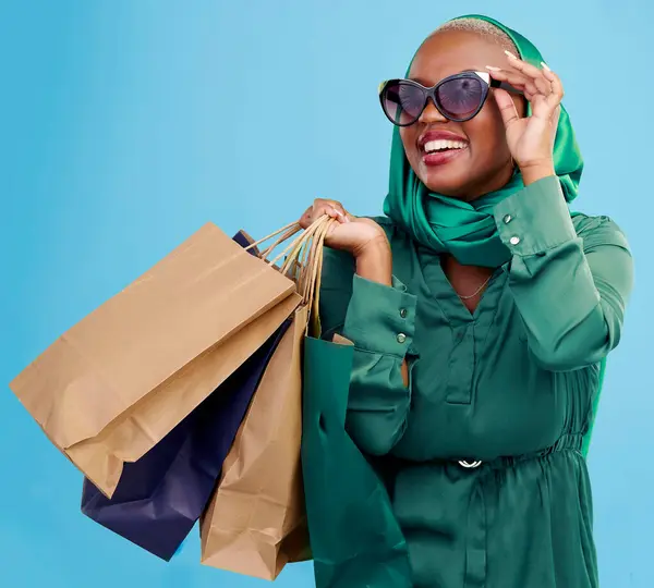 Shopping, sunglasses and black woman with bags, retail and luxury items on a blue studio background. African person, customer and model with expensive clothes, client and boutique products with sales.