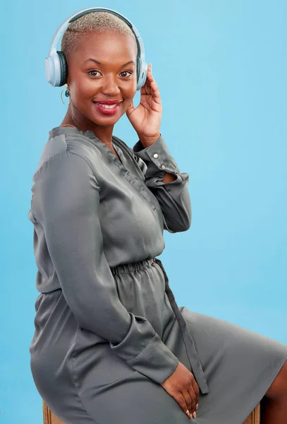 Black woman, headphones and music in studio portrait, smile and listening to radio by blue background. African girl, audio tech and streaming subscription service with sound, hearing and relax.