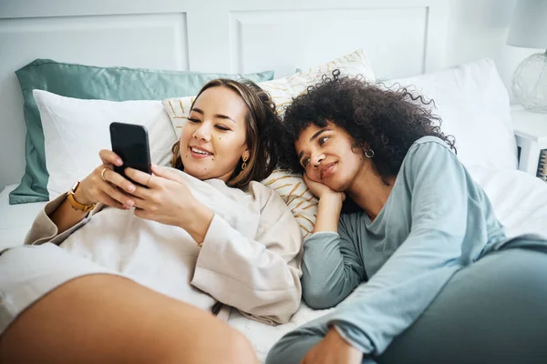 stock image Phone, love and a lesbian couple in bed together in the morning for communication or to relax. Social media, lgbt and a woman watching a movie or video with her girlfriend in the home bedroom.