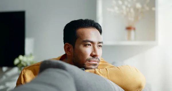 stock image Thinking, memory and sad asian man on a sofa with nostalgia, depression or grief in his home. Burnout, worry and Japanese male in living room with broken heart, mourning or anxiety for loss and debt.