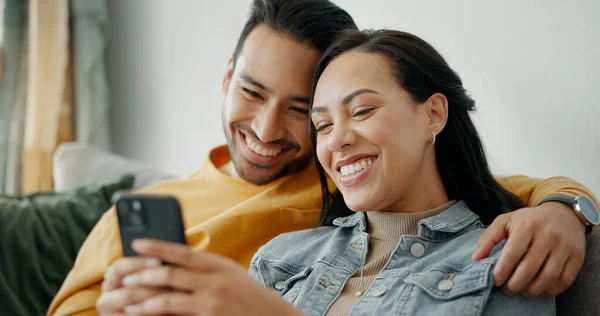 Couple, smile and talking on sofa with phone for social media post, subscription and reading funny notification. Happy man, woman and hug with smartphone for meme, games app and relax in living room.