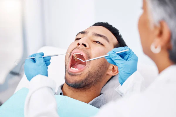 Dentist, patient man and consultation for mouth and teeth whitening, cleaning or veneers hygiene. Oral health, orthodontics and a person for tooth care, dental assessment and mirror tools at clinic.
