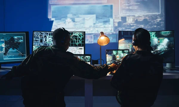Army control room, computer and team in surveillance, help and collaboration in tech communication from back. Security, satellite map and man with woman at monitor in military office command center