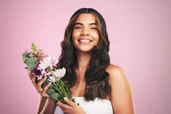 Happy woman, flowers and portrait in studio for skincare, natural cosmetics and aesthetic shine on pink background. Model smile for eco beauty with floral plants, sustainable dermatology and bouquet.