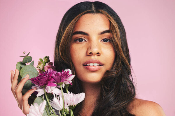 Face of woman, flowers and portrait in studio for skincare, natural spring cosmetics and aesthetic shine on pink background. Model, eco beauty and bouquet of floral plants for sustainable dermatology.